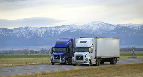 Two semi trucks hauling trailers along a mountain highway in West Virginia