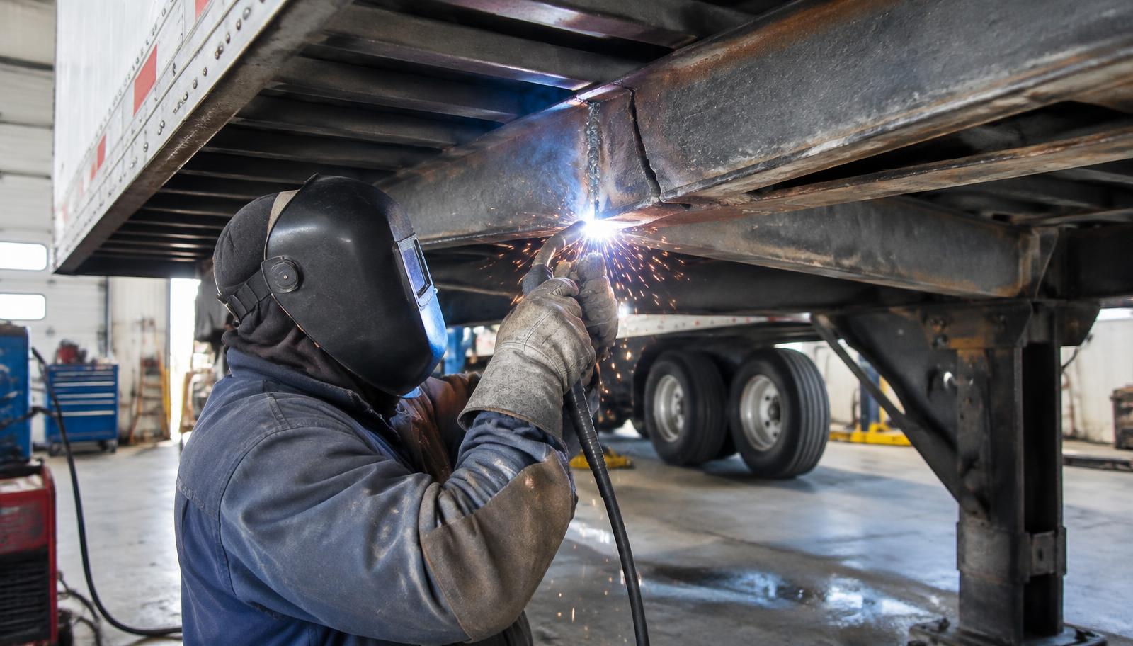 Welder repairing a cracked semi trailer frame crossmember in the shop
